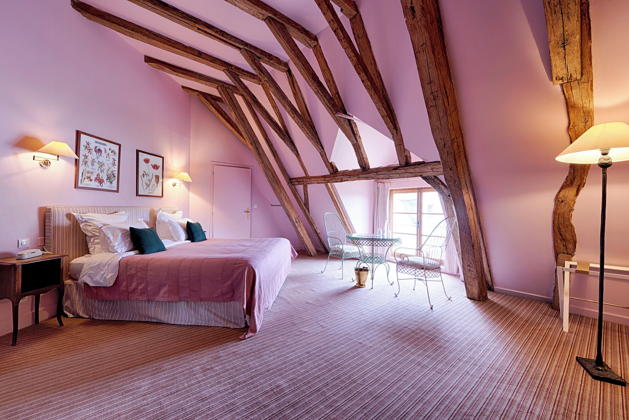 A bedroom with a sloped ceiling, a bed, a bedside table, a chair, and a table with a lamp.