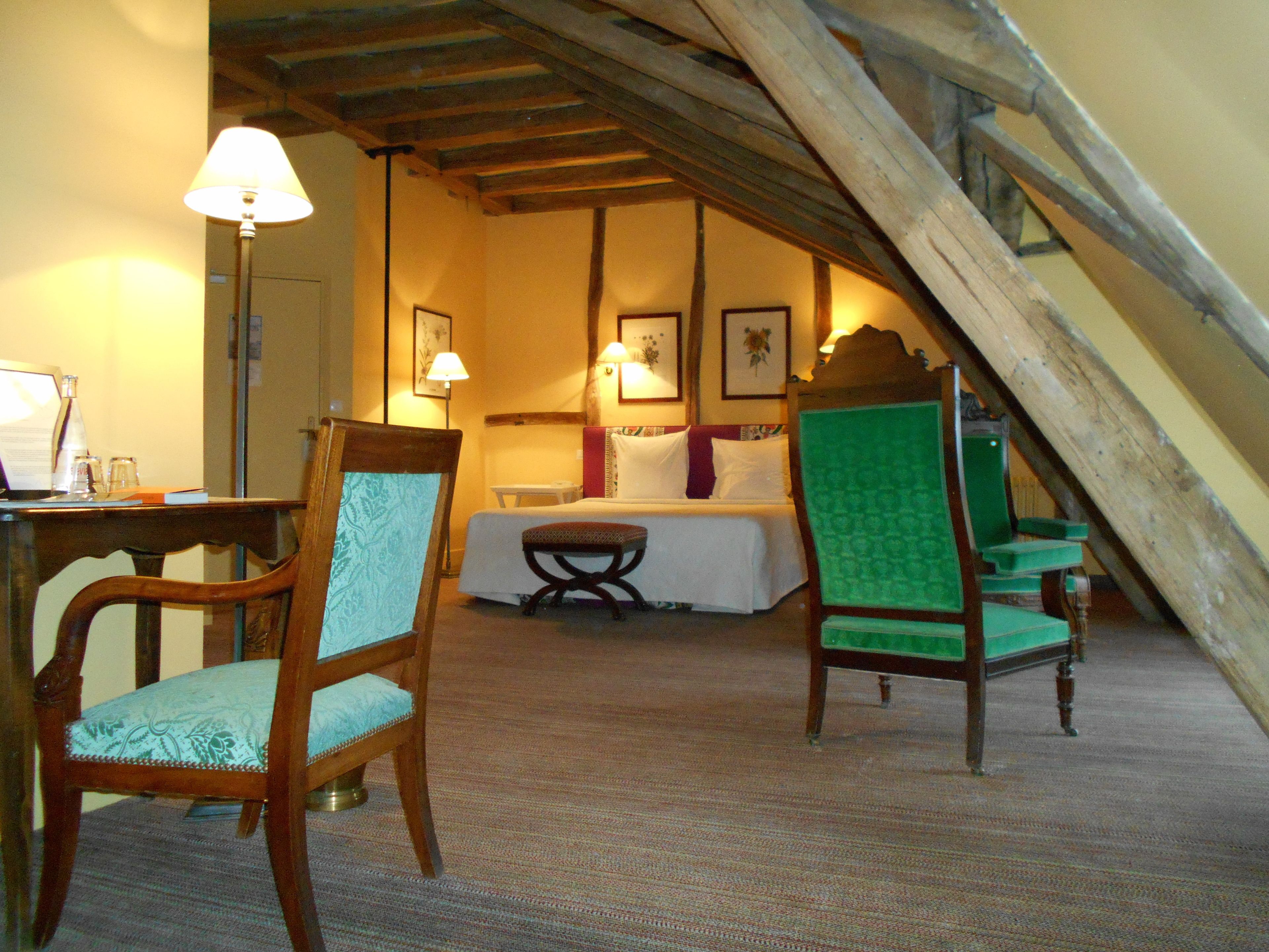 A cozy room with a bed, two chairs, a table, and a lamp.