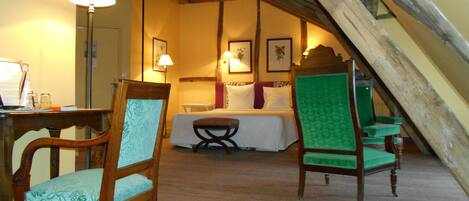 A cozy room with a bed, two chairs, a table, and a lamp.