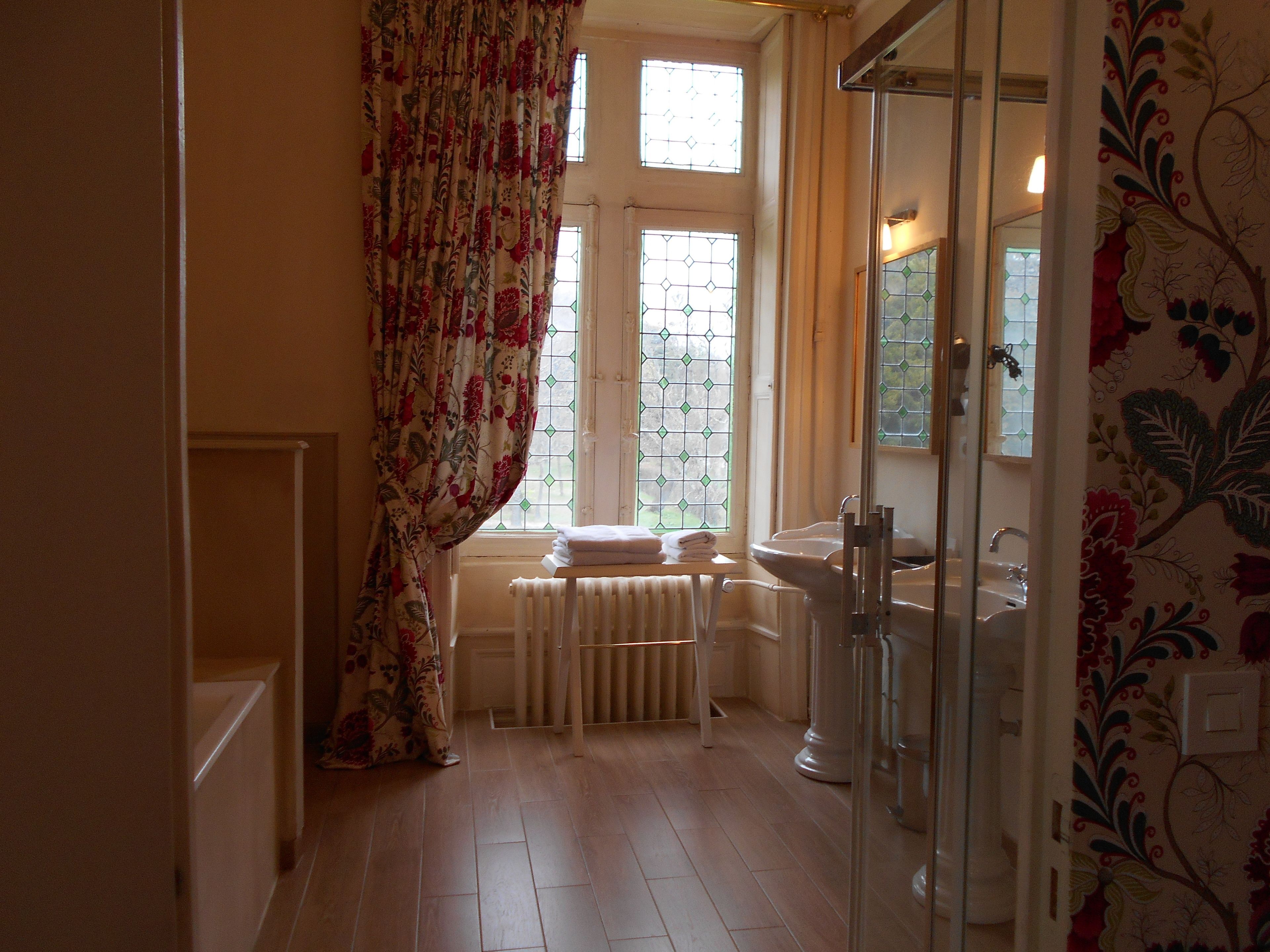 Een badkamer met een radiator, een wastafel en een raam met bloemen gordijnen.