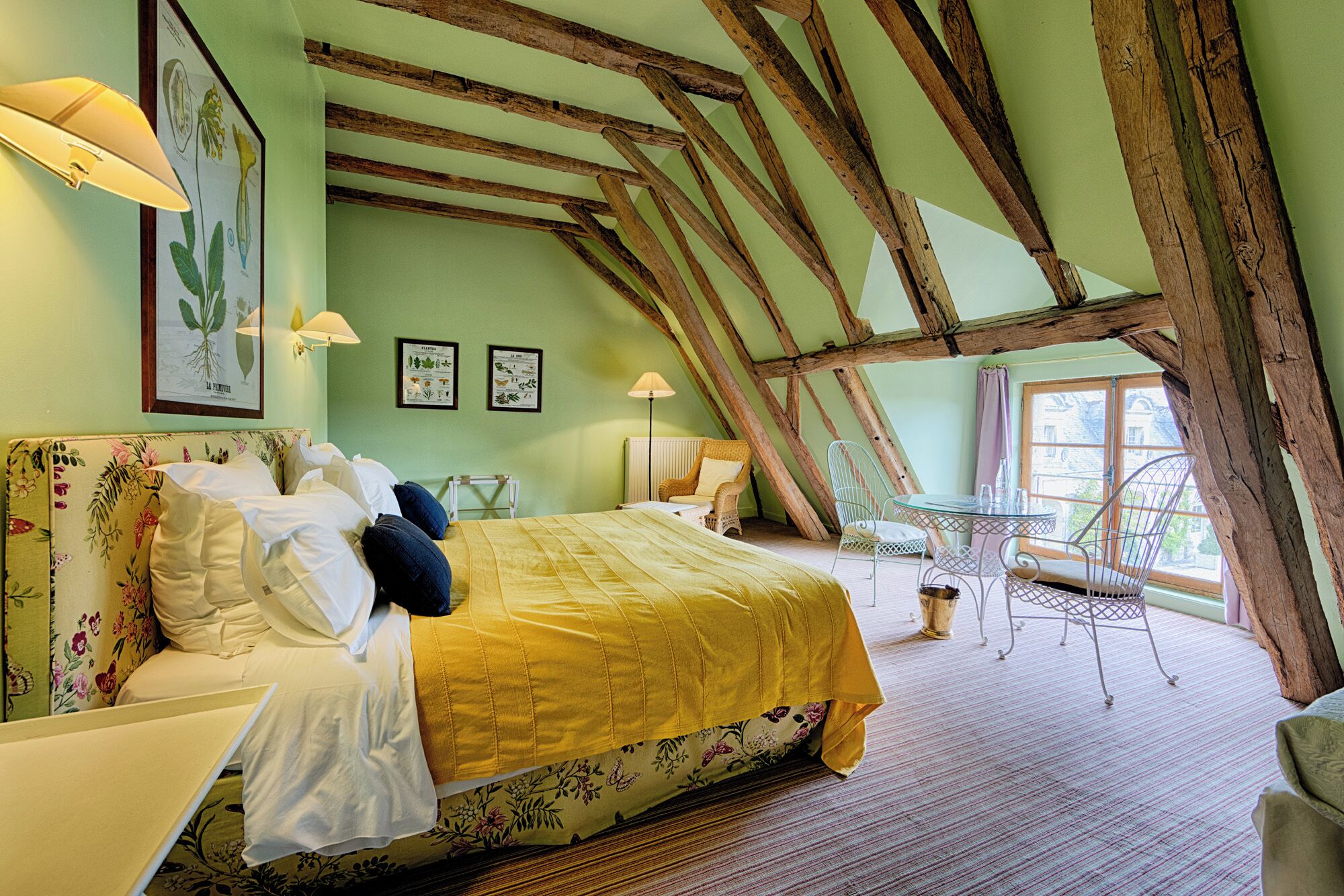 Un dormitorio con cama, una silla, una mesa y un ventanal.