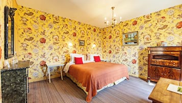 A room with floral wallpaper, a bed with red and white bedding, a wooden dresser, and a chandelier.