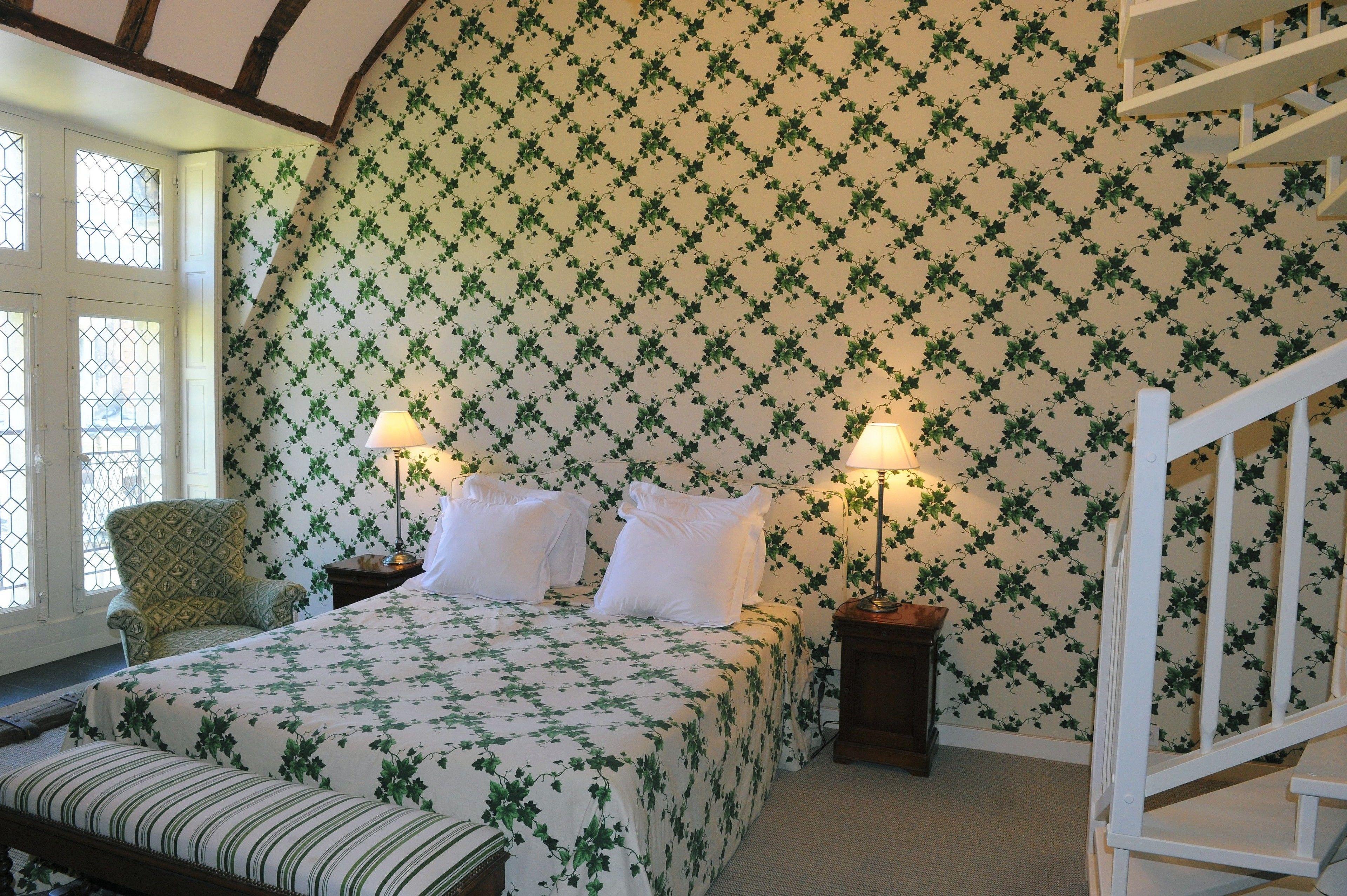 Une chambre avec un lit, deux tables de chevet, une chaise et un escalier blanc.