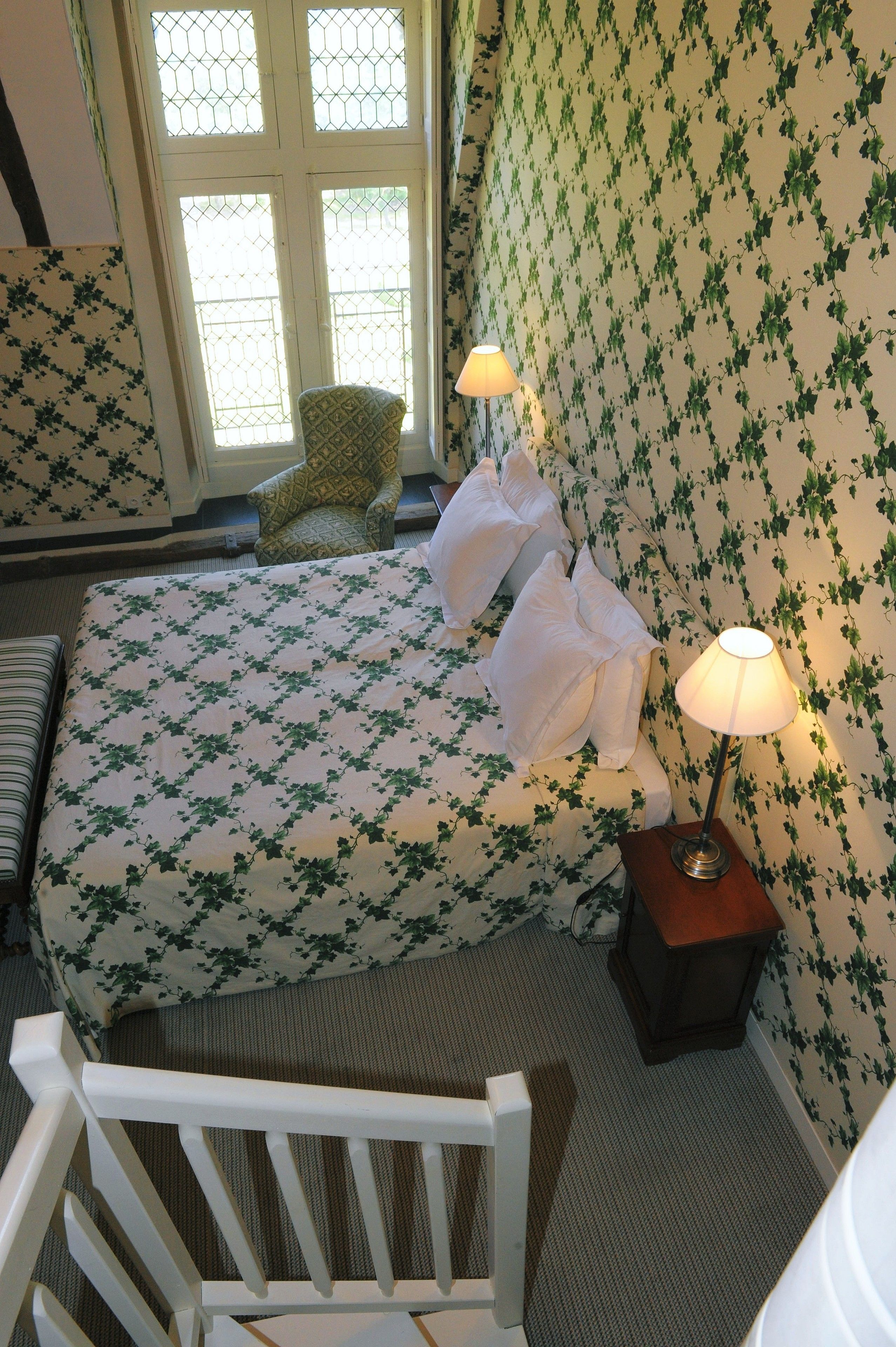 A hotel room with a bed, a chair, a lamp, and a window.