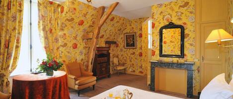 Habitación de hotel con papel tapiz floral, una cama con una bandeja de desayuno, chimenea y candelabro.