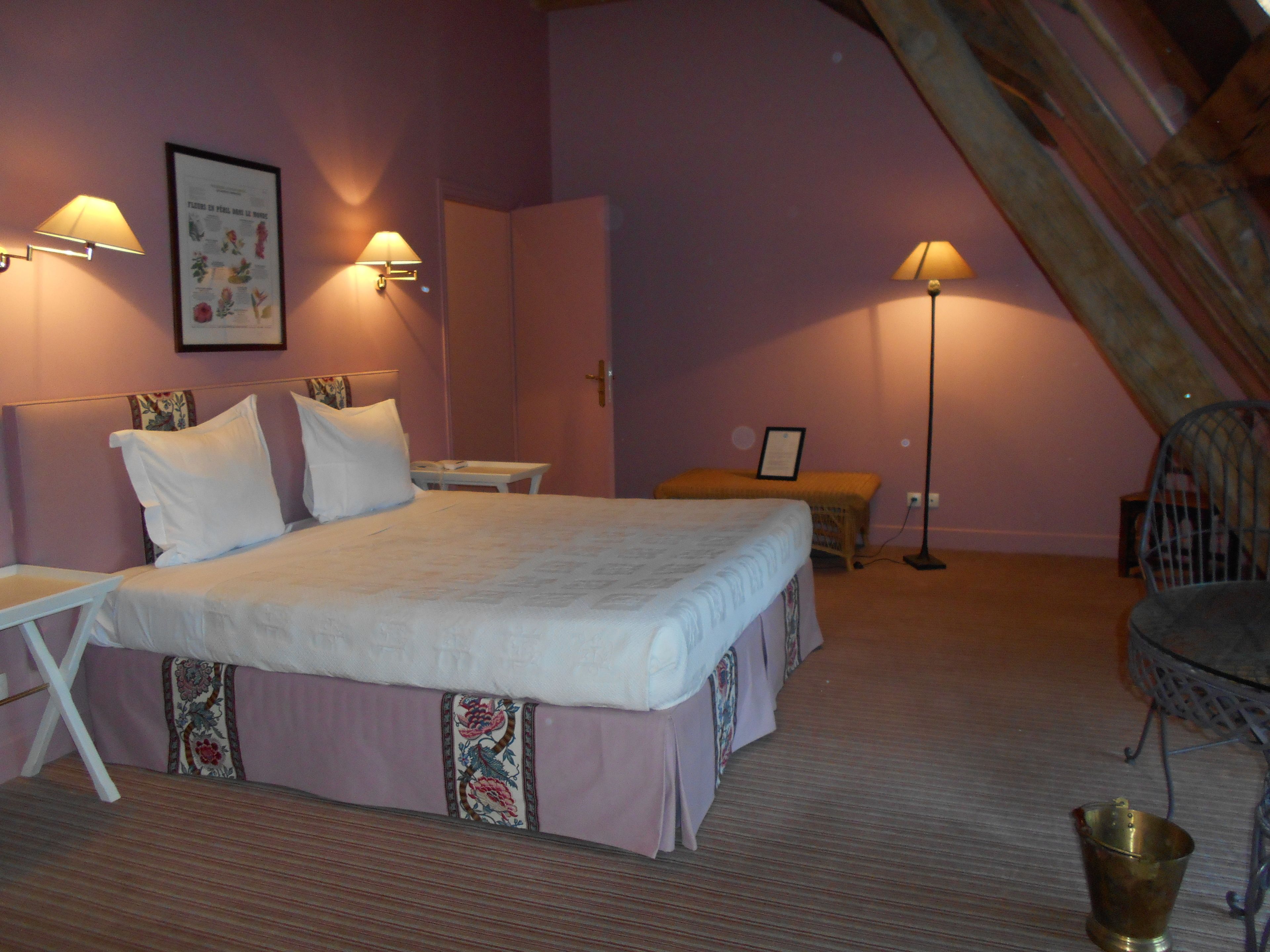 A bedroom with a large bed, bedside lamps, a framed floral artwork, a small table, and a chair.