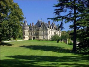 A large, historic building with a symmetrical facade, multiple chimneys, and a well-maintained lawn.