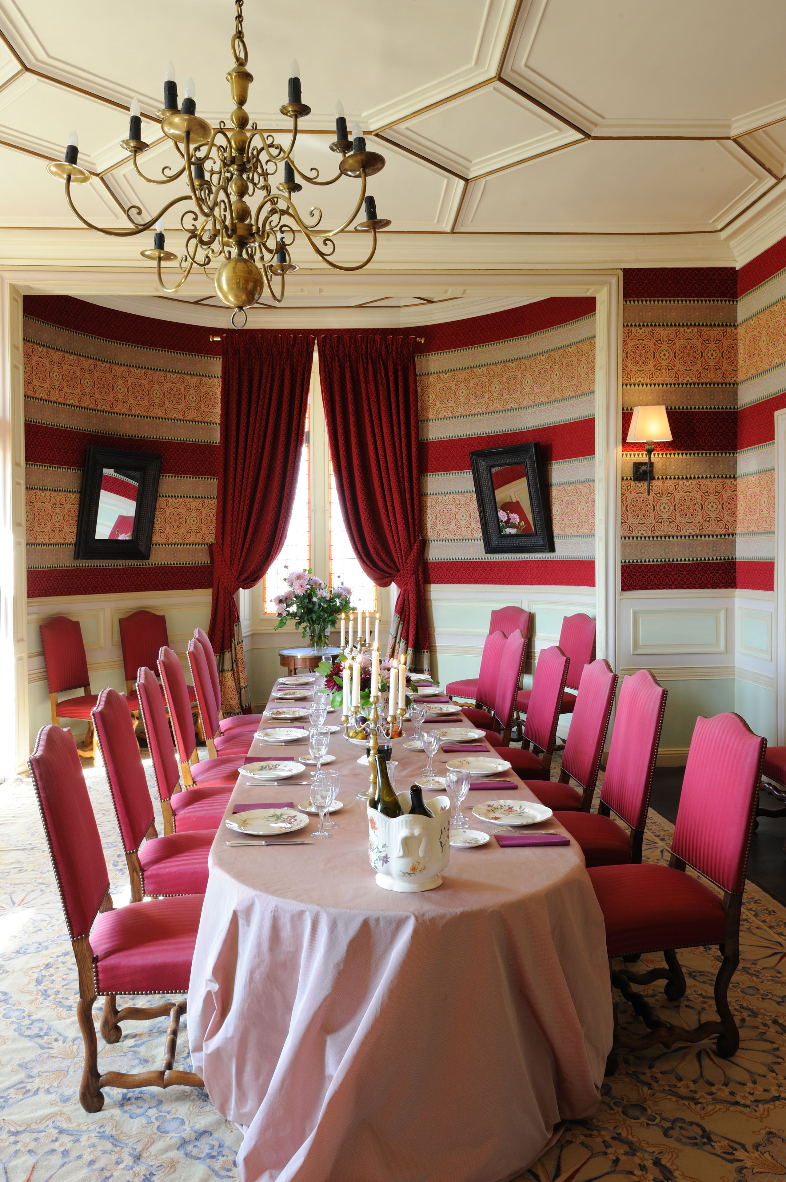 Comedor formal con una larga mesa dispuesta para una comida, sillas tapizadas en rojo y un candelabro.
