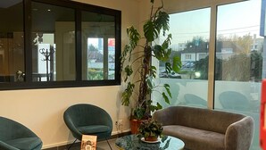 A modern living room with a glass table, two green armchairs, a brown sofa, and a large potted plant. - Kyriad Saint Fargeau Ponthierry Apollonia (Saint-Fargeau-Ponthierry)