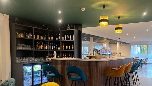 A bar area with a counter, stools, and shelves of bottles and glasses. - Kyriad Saint Fargeau Ponthierry Apollonia (Saint-Fargeau-Ponthierry)
