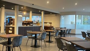 A modern cafe with multiple tables and chairs, a counter with a coffee machine, and large windows providing natural light. - Kyriad Saint Fargeau Ponthierry Apollonia (Saint-Fargeau-Ponthierry)