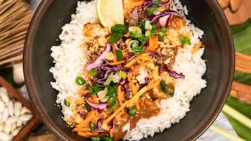 A bowl of rice topped with shredded carrots, red cabbage, and green onions, garnished with a slice of lime.