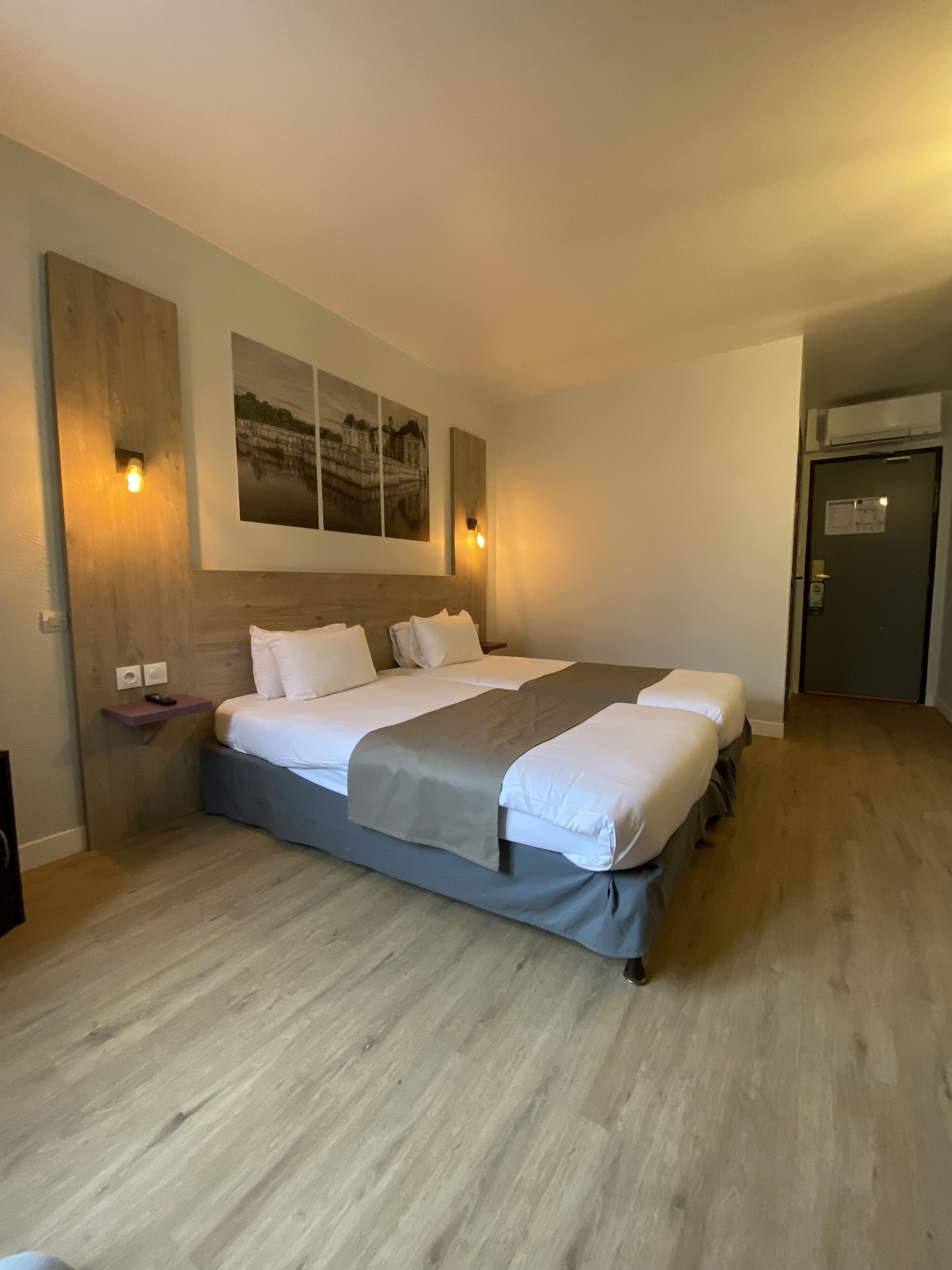 A double bed with a grey bedspread, two bedside tables, and a wall-mounted light fixture.