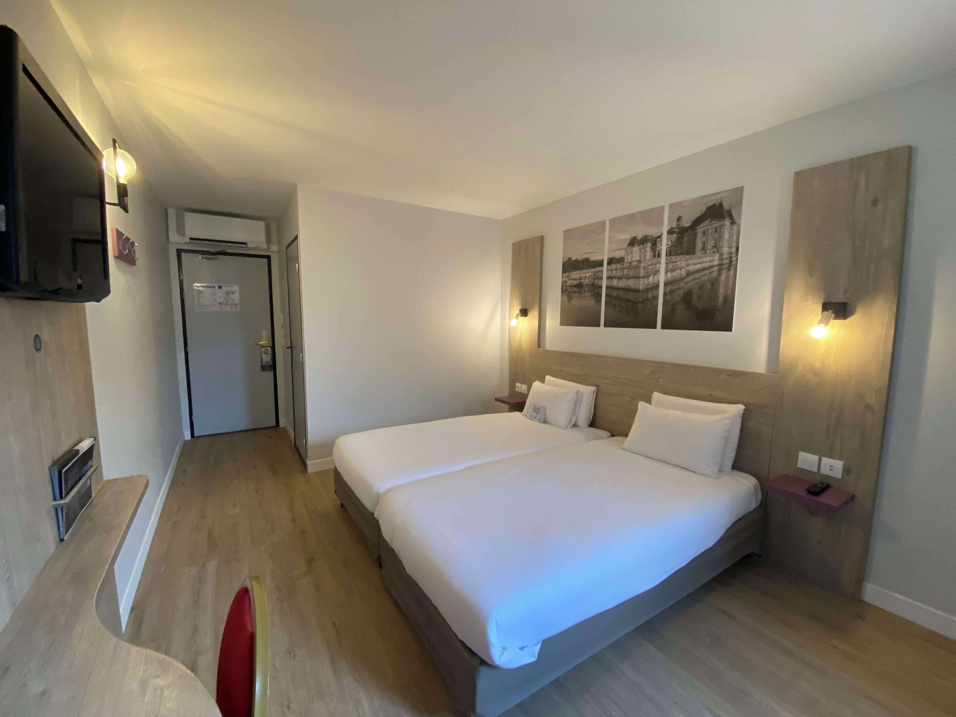 Una camera d'albergo con un letto grande, una TV fissata al muro e un pavimento in legno.