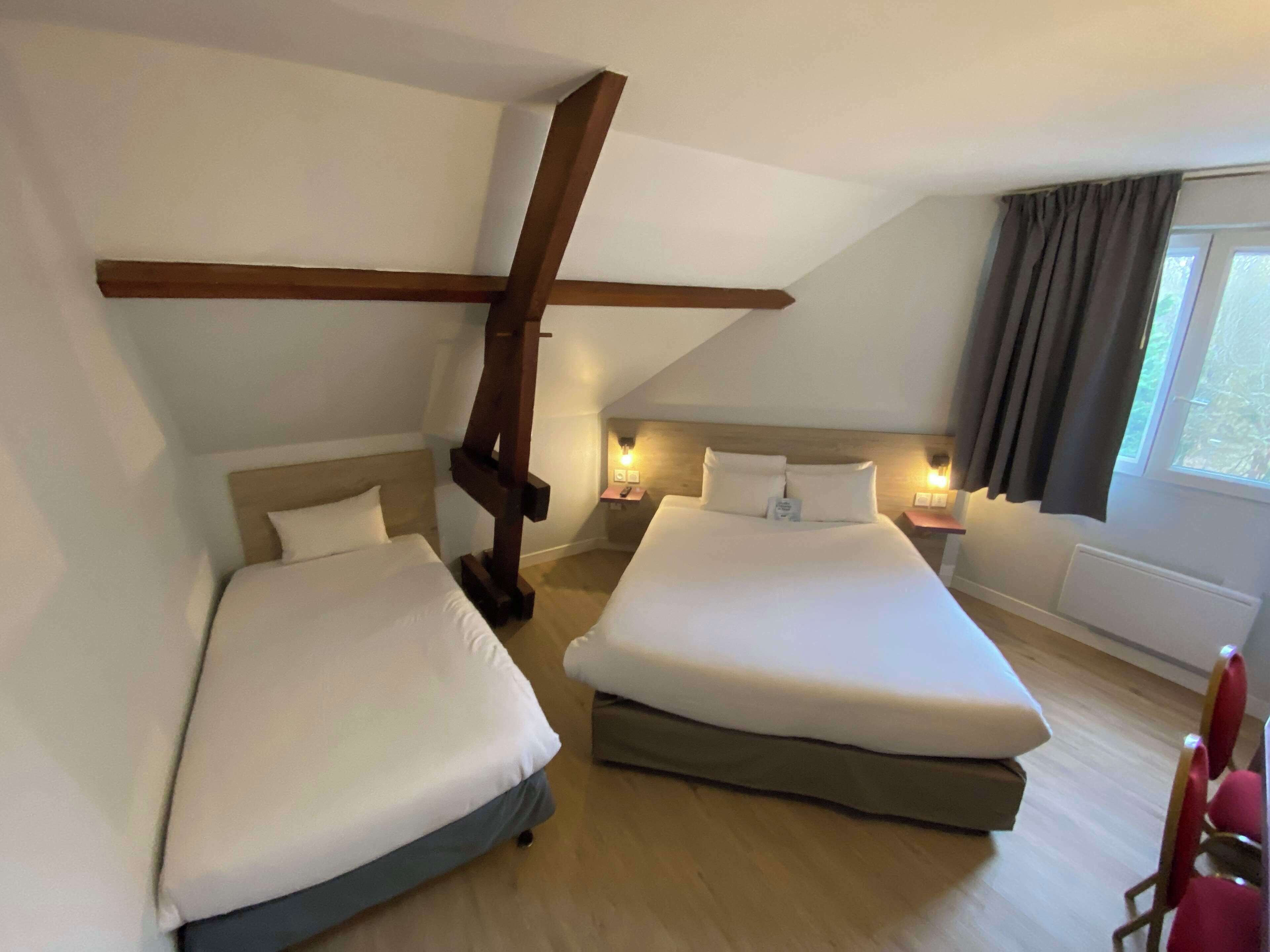 Una habitació d'hotel amb dos llits, bigues de fusta, una finestra amb cortines i làmpades laterals.