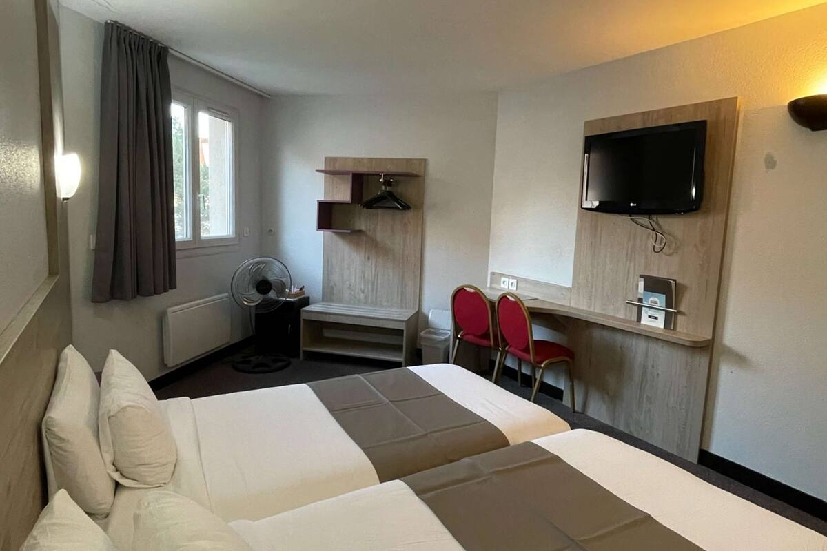 A hotel room with two beds, a desk, a chair, a TV, and a window with curtains.