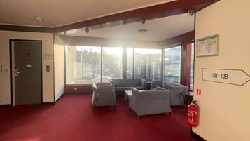 A spacious lobby with red carpet, grey sofas, and a fire extinguisher on the wall.