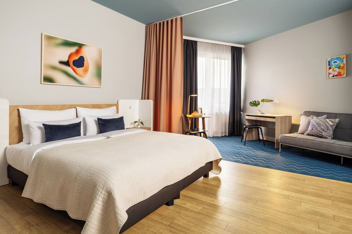 Quarto de hotel com uma cama grande, uma escrivaninha, um sofá e uma poltrona.