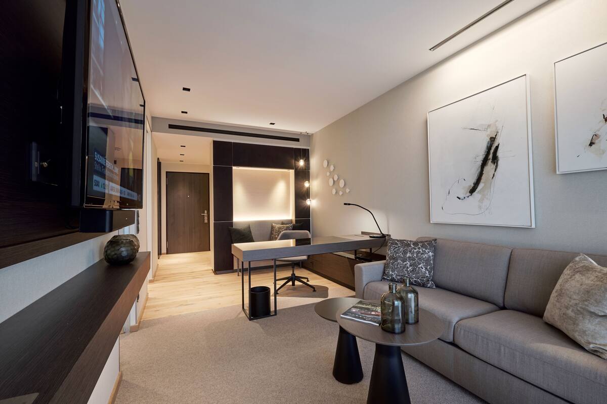 En moderne stue med sofa, sofabord og et skrivebord med lampe. Der er et stort vindue og kunst på væggen.