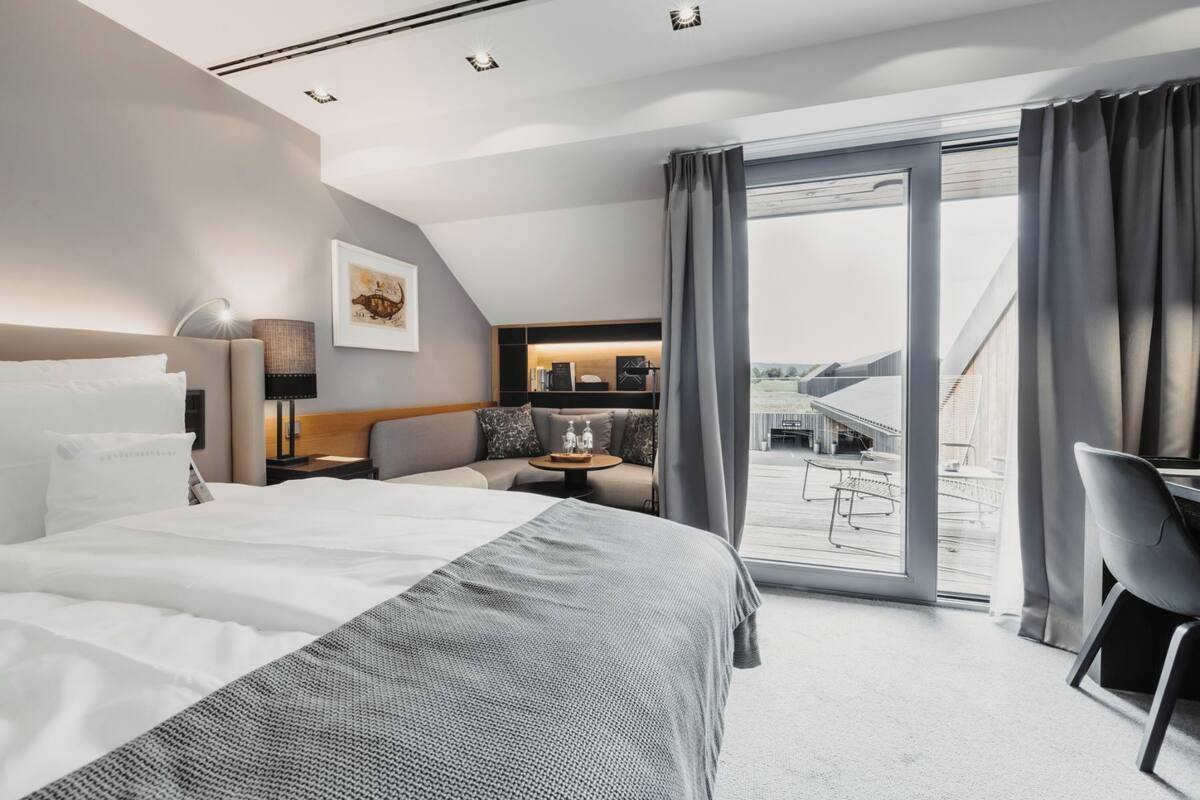 Et moderne hotelværelse med en stor seng, et skrivebord, en stol og en balkon med udsigt.