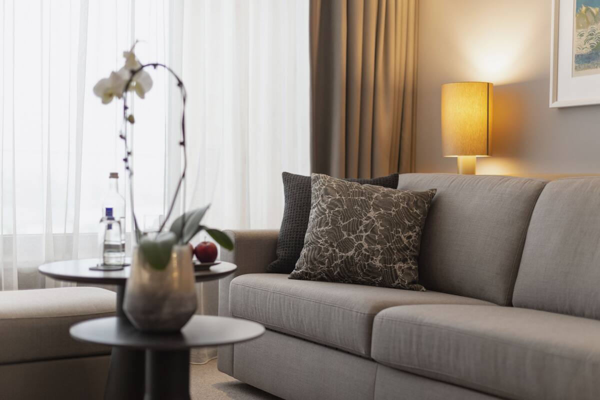 En moderne stue med sofa, et rundt bord med en vase og en flaske, samt en lampe.