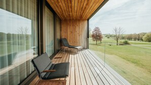 A balcony with two chairs, wooden flooring, and a view of a grassy landscape. - Severin*s Resort & Spa Öschberghof (Donaueschingen)
