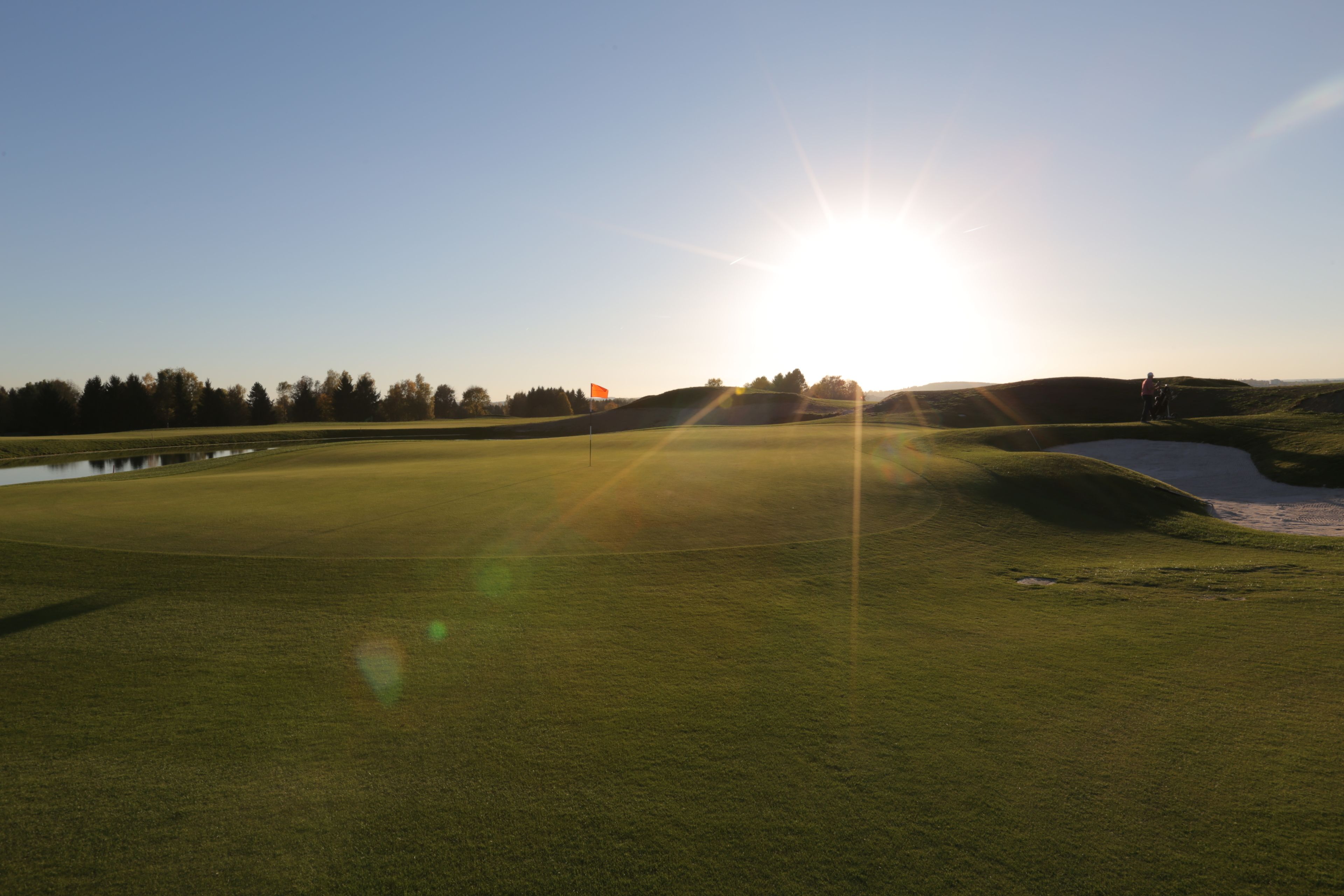 A golf course with a clear sky, a flag, and a body of water.