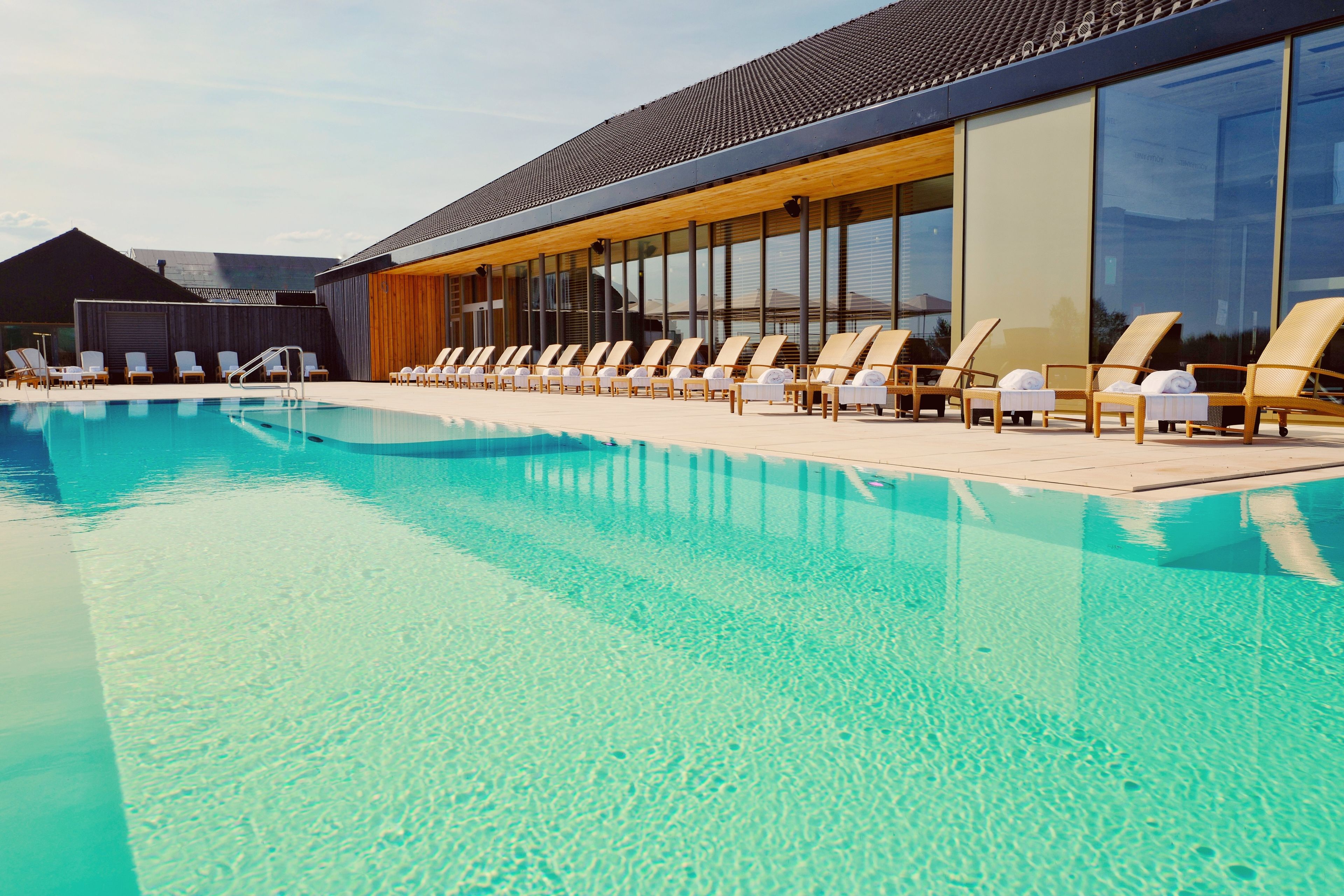 Un área de piscina moderna con sillones de descanso y un edificio con amplias ventanas.