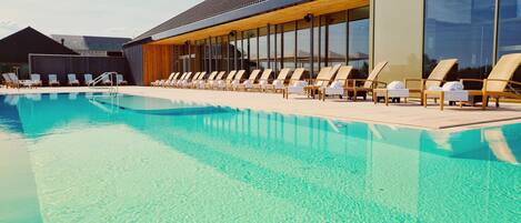 Un área de piscina moderna con sillones de descanso y un edificio con amplias ventanas.