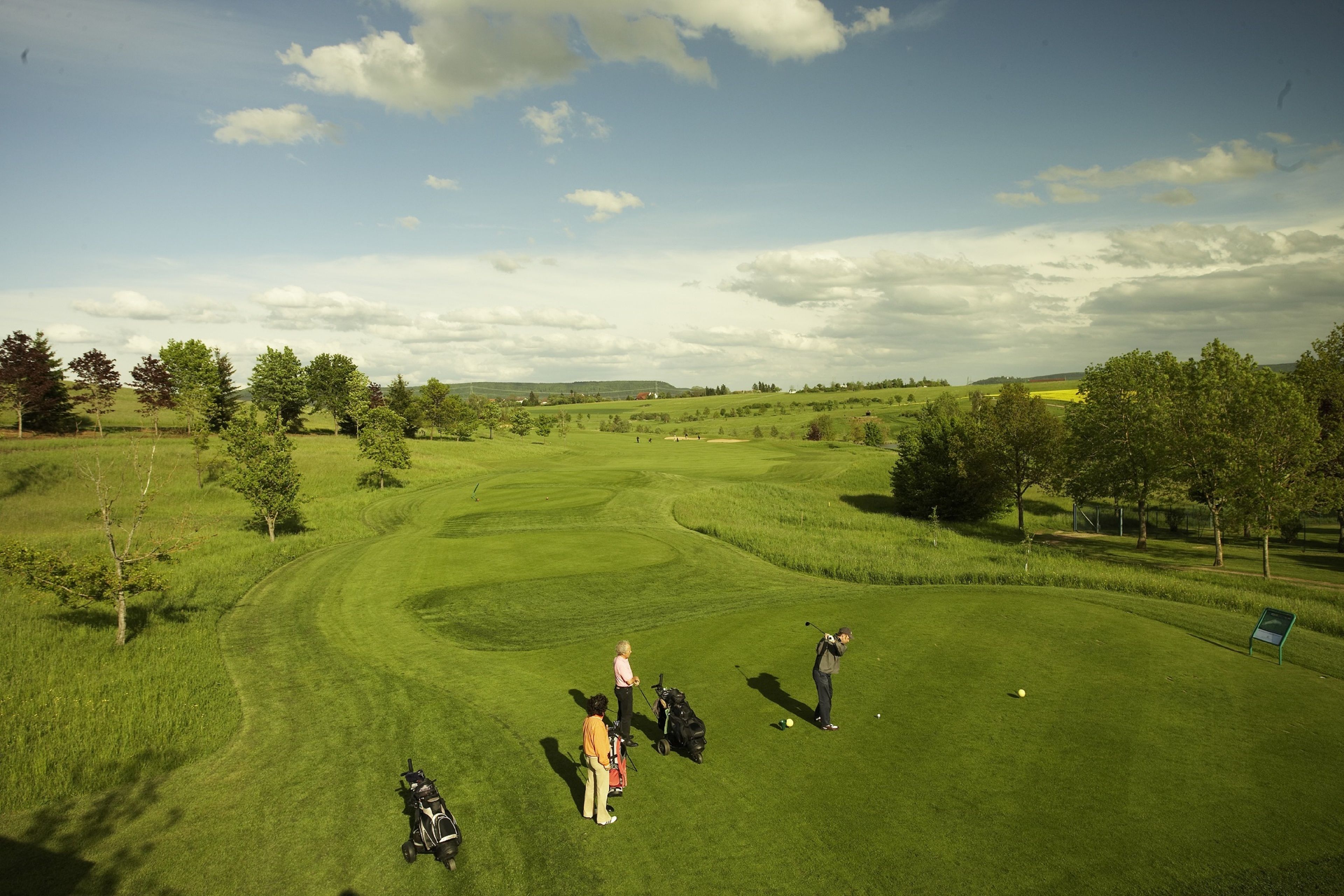 Un campo de golf con cielo despejado, césped verde y árboles.