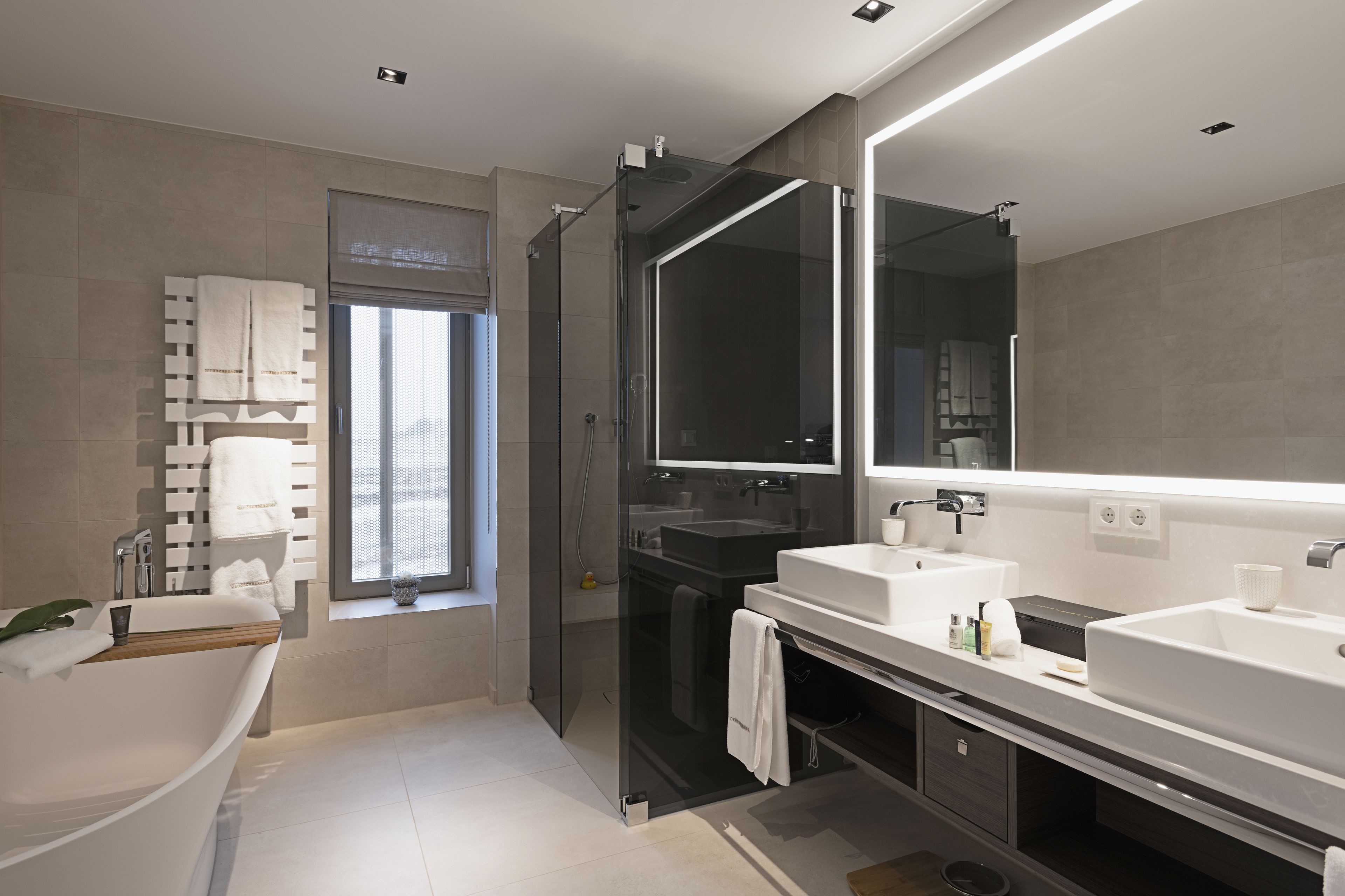 Un baño moderno con ducha de vidrio, una bañera independiente y un espejo grande sobre el lavabo.