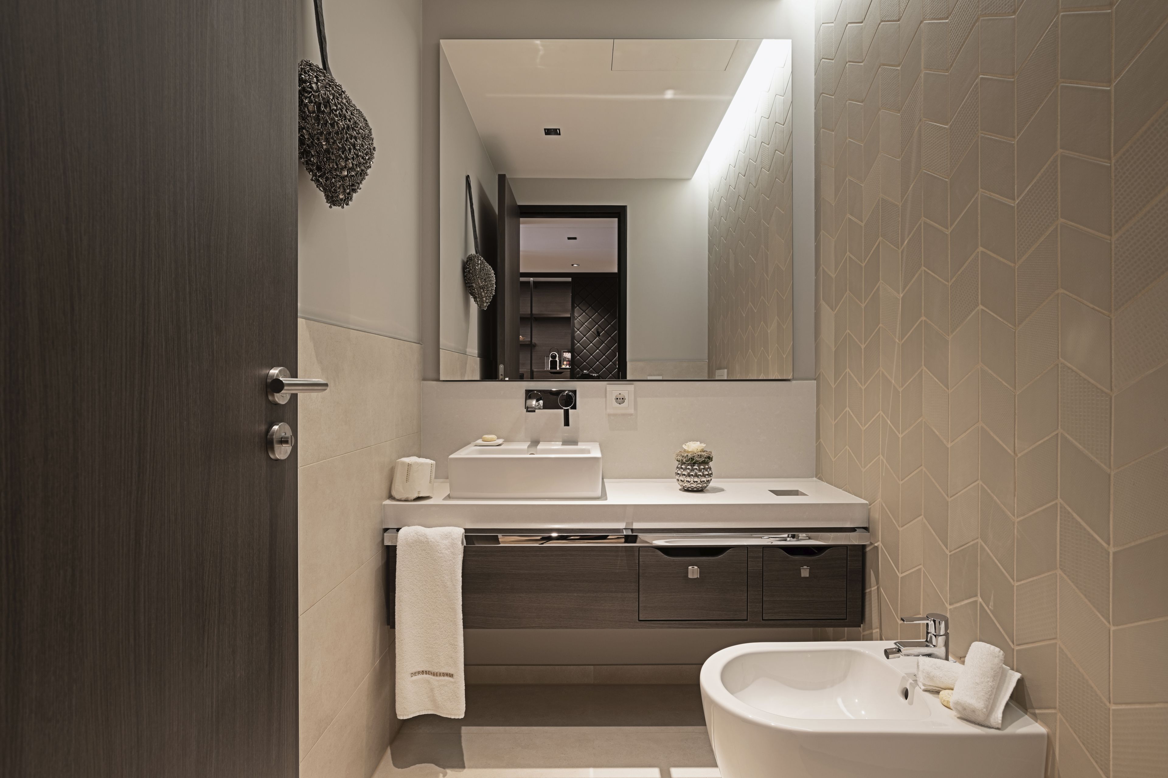 A modern bathroom with a large mirror, a sink, a vanity with drawers, and a bathtub.