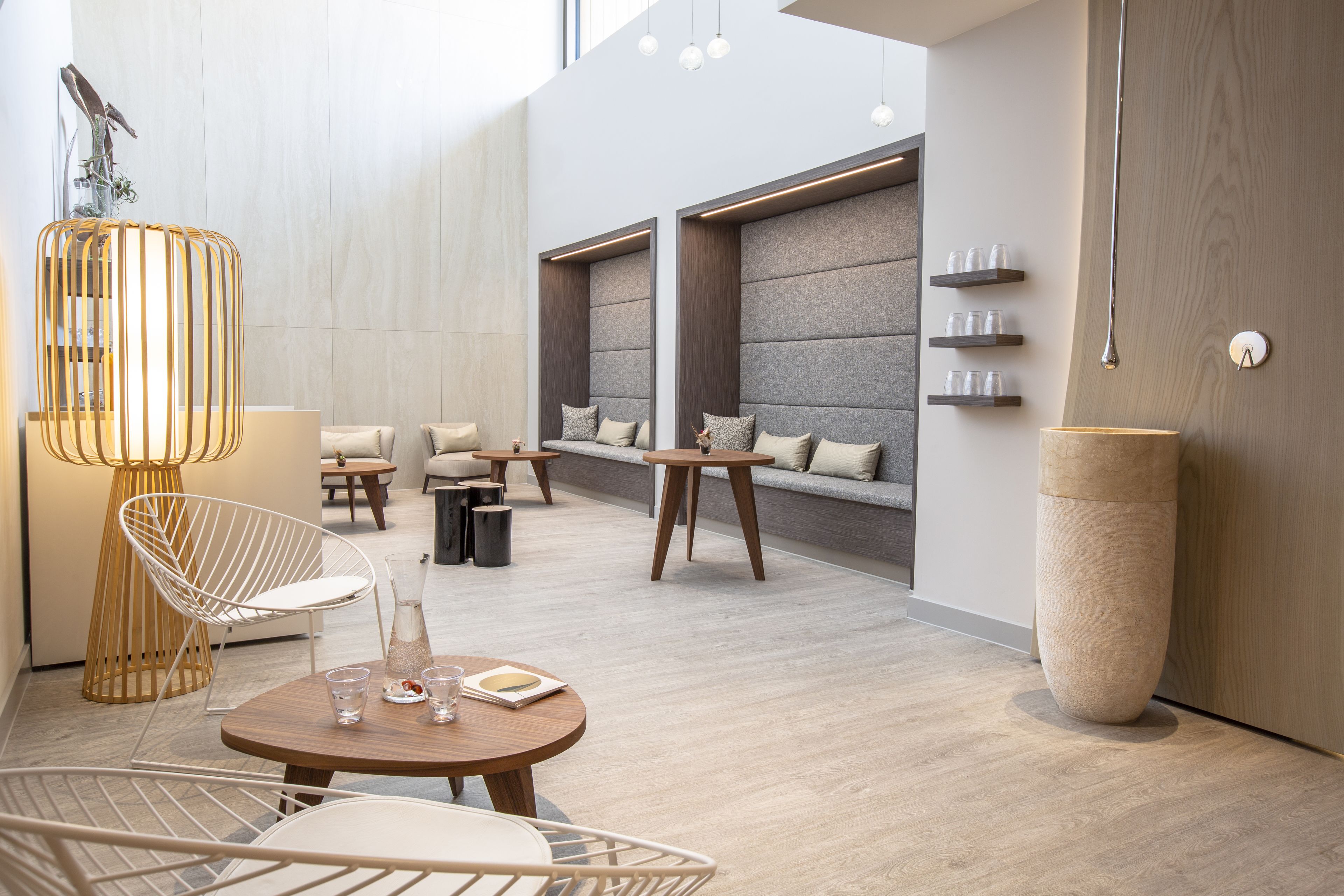 A modern lounge area with a round wooden table, white wire chairs, and a seating area with sofas and a wall-mounted shelf.