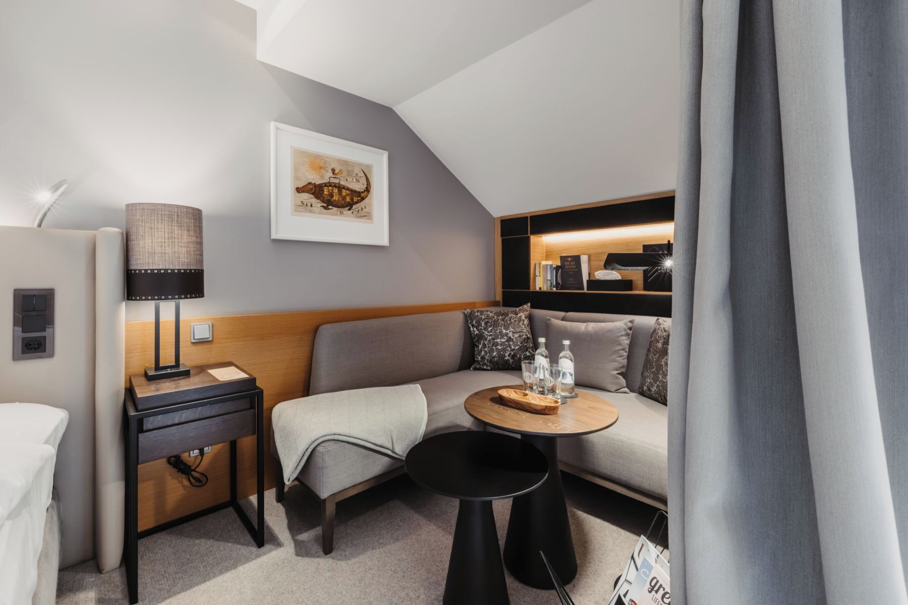 Ein modernes Hotelzimmer mit einer Couch, einem kleinen runden Tisch, einer Lampe und einem gerahmten Bild an der Wand.