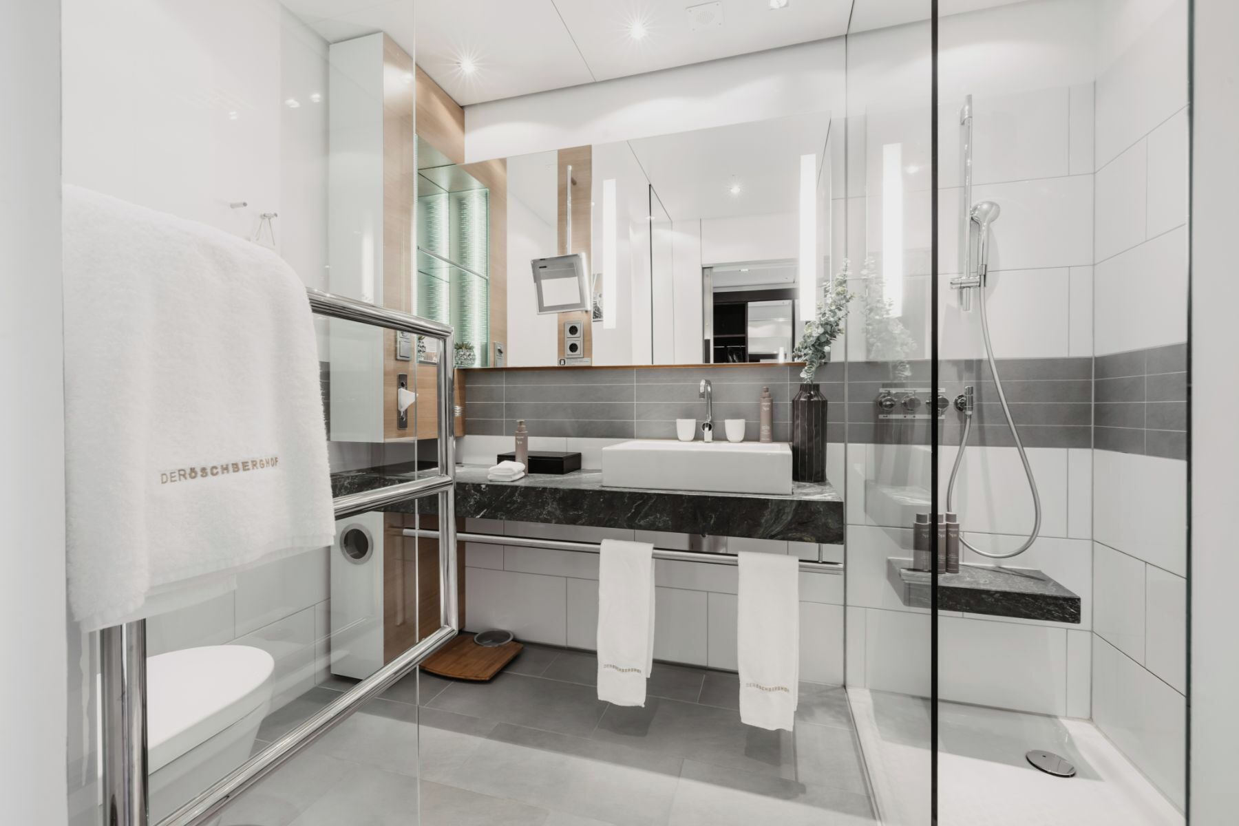 A modern bathroom with a glass shower enclosure, a white sink, and a marble countertop.