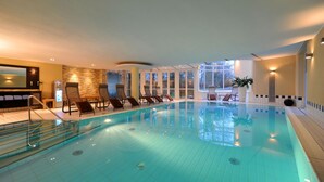 A large indoor swimming pool with multiple lounge chairs and a stone wall. - Hotel Caroline Mathilde (Celle)