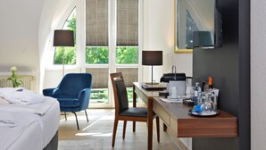 A hotel room with a bed, a desk, a chair, a TV, and a window with blinds. - Hotel Caroline Mathilde (Celle)