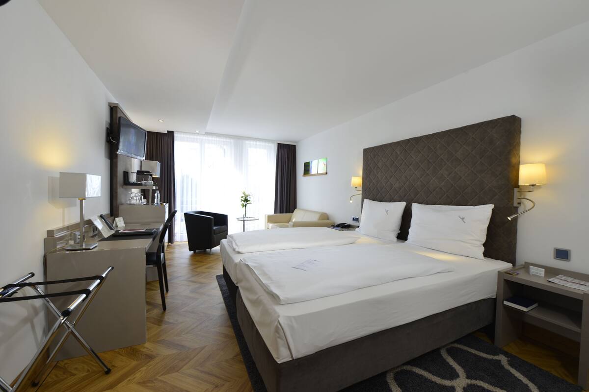 A hotel room with a large bed, a desk, a chair, and a TV.