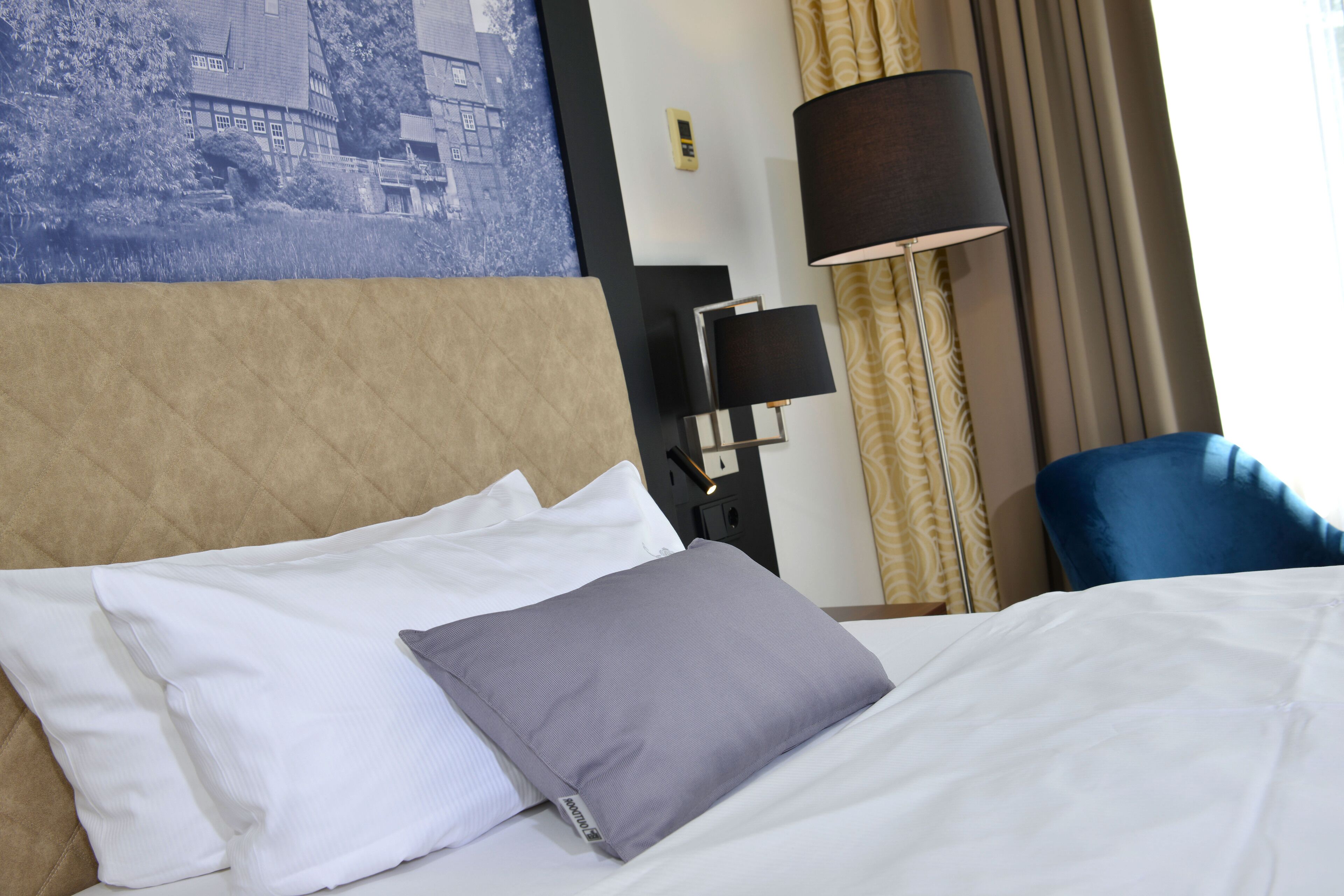 Habitación de hotel con cama, cabecero, lámpara, una silla y teléfono en la pared.