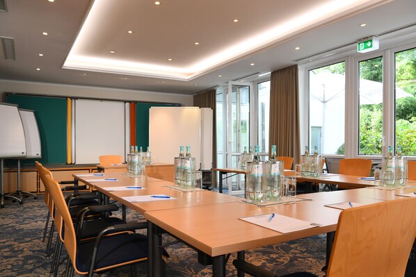 A conference room with a long table, chairs, a whiteboard, and large windows with curtains.