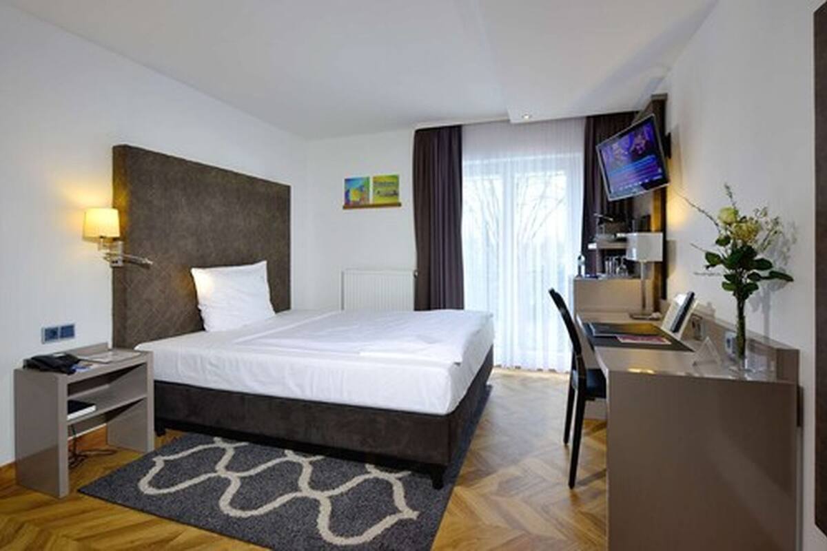 A modern hotel room with a large bed, a desk, a TV, and a small desk area.