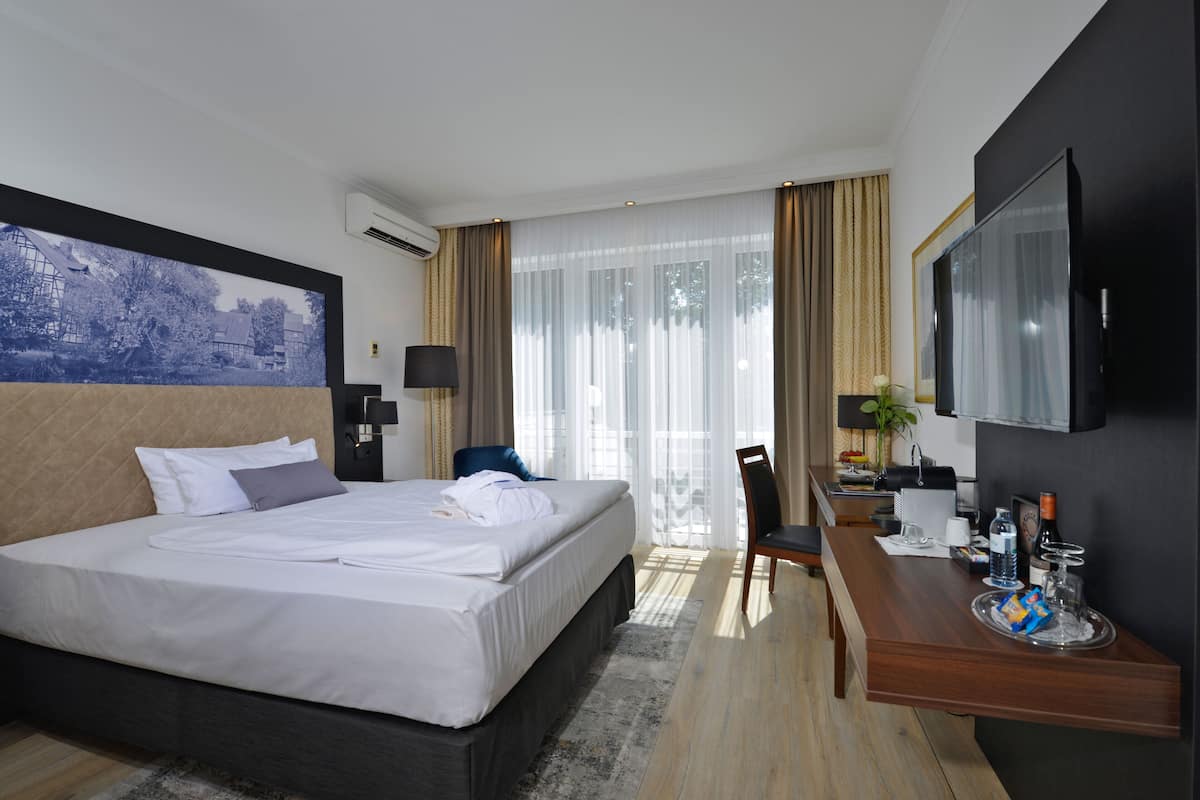 A hotel room with a large bed, a desk with a chair, a television, and a window with curtains.
