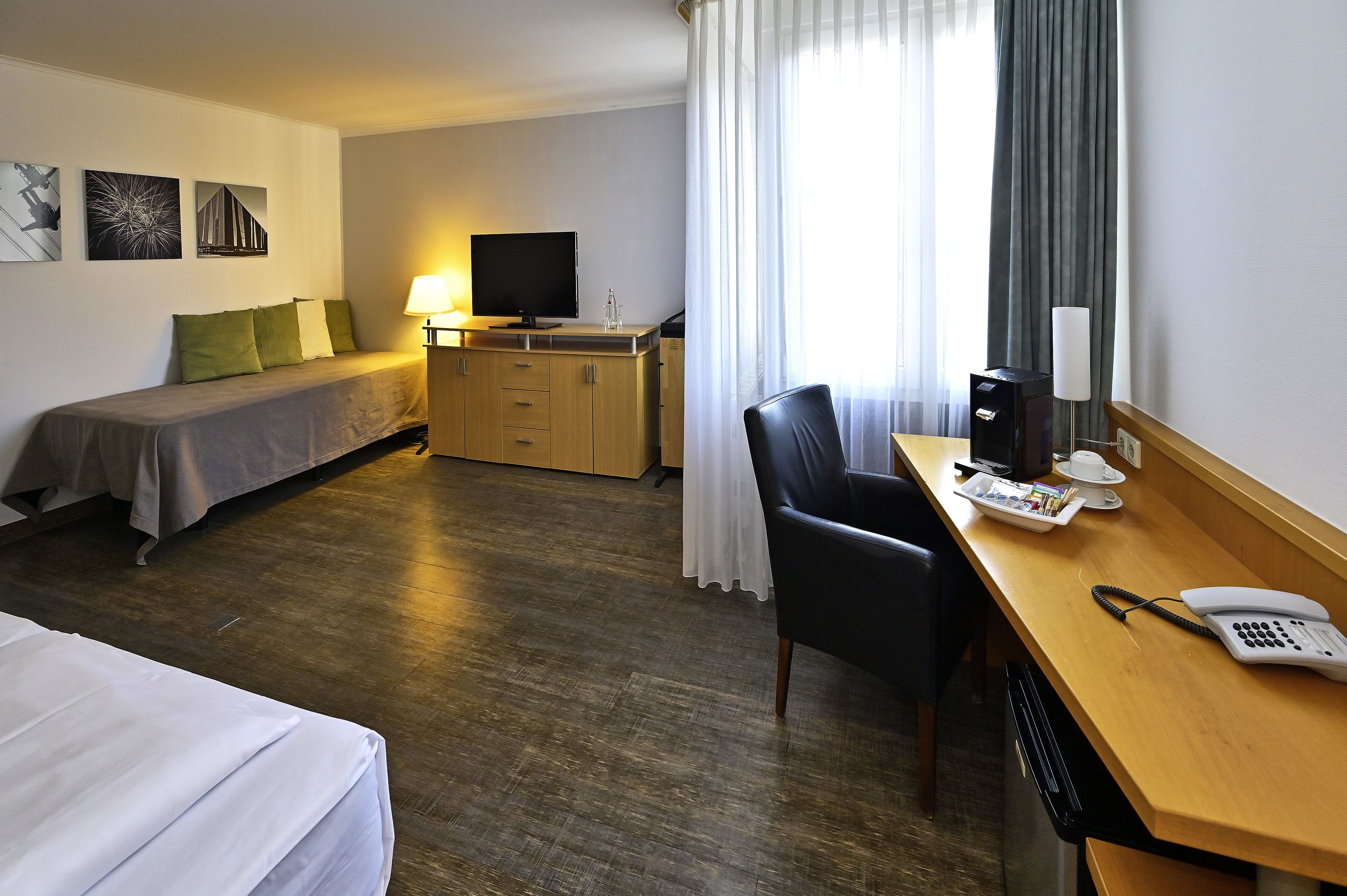 Una habitación de hotel con una cama, un escritorio con teléfono, una silla, un televisor y una ventana con cortinas.