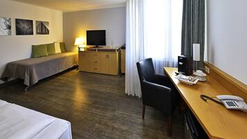 Una habitación de hotel con una cama, un escritorio con teléfono, una silla, un televisor y una ventana con cortinas.