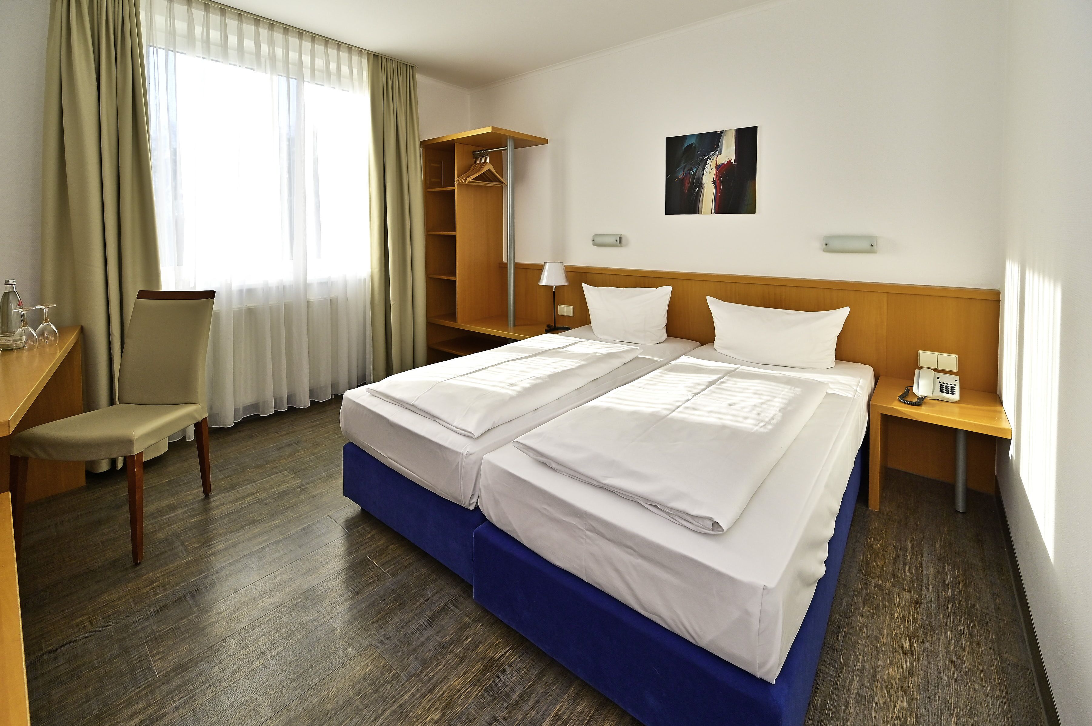 Habitación de hotel con cama doble, escritorio con silla, armario y mesita de noche con lámpara y teléfono.