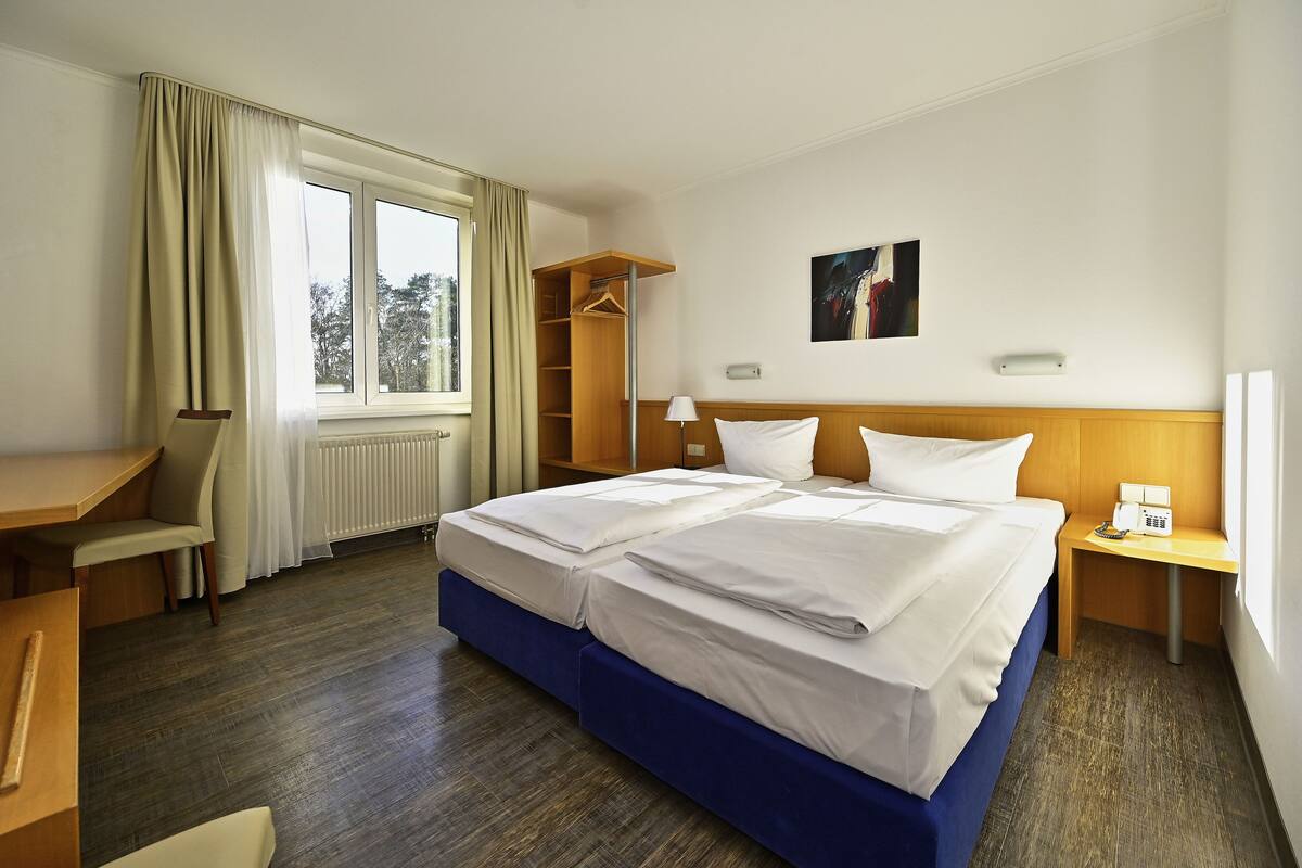 A hotel room with a large bed, a desk, a chair, a wardrobe, and a window with curtains.