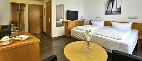 Habitación de hotel con cama, escritorio con computadora, televisión y un cuadro en la pared.