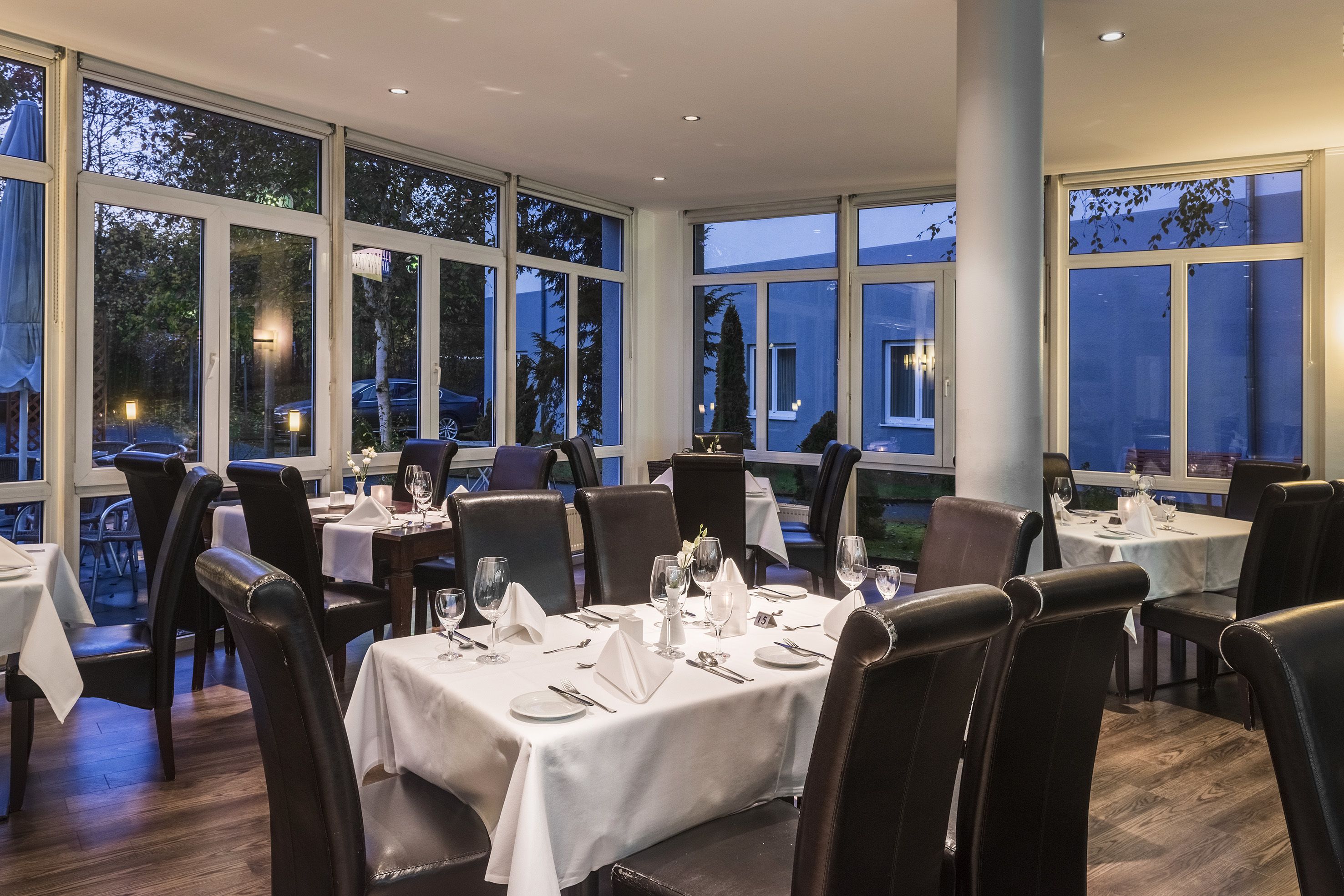 A restaurant with multiple tables set for dining, large windows, and a view of the outside.