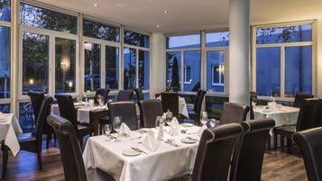 A restaurant with multiple tables set for dining, large windows, and a view of the outside.