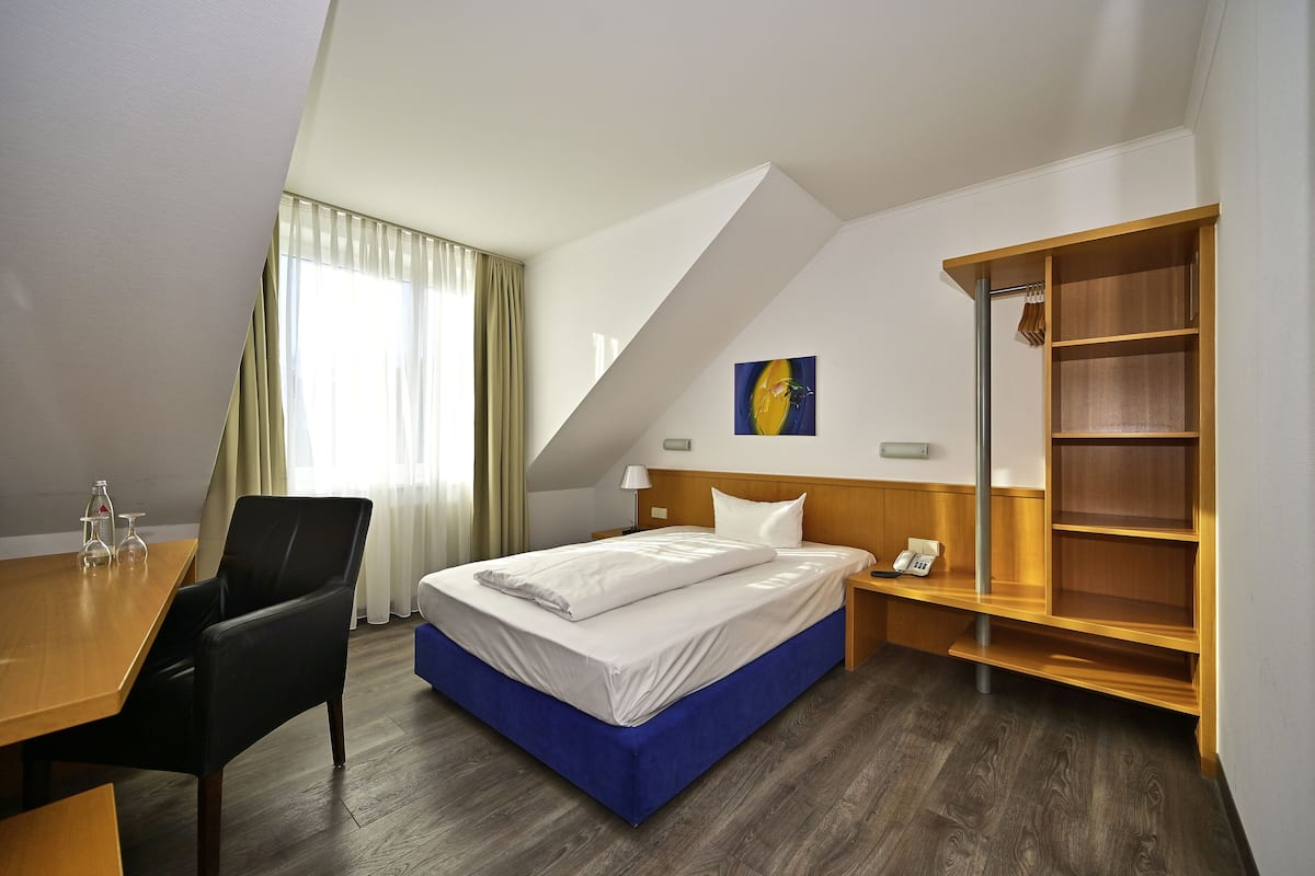 A hotel room with a bed, a desk, a chair, a wardrobe, and a window with curtains.